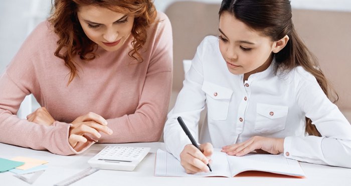 Girl writing in notebook near mother and calculator on table