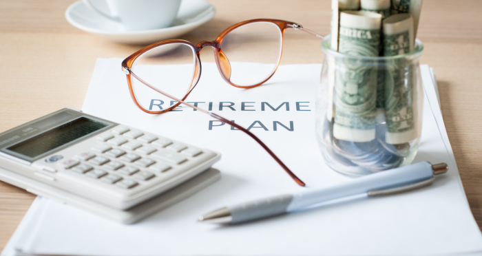 Desk with retirement plan document, calculator, glasses, coffee, money in jar