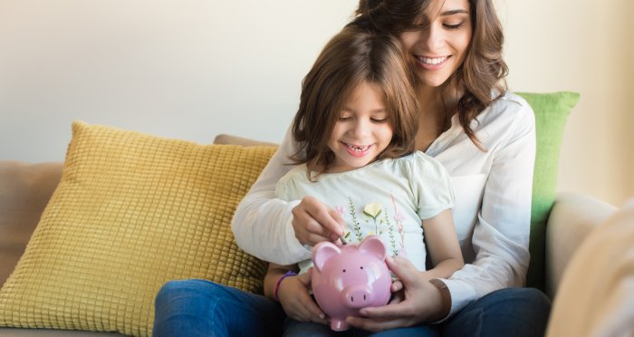 Mother teaching young daughter about money holding piggy bank